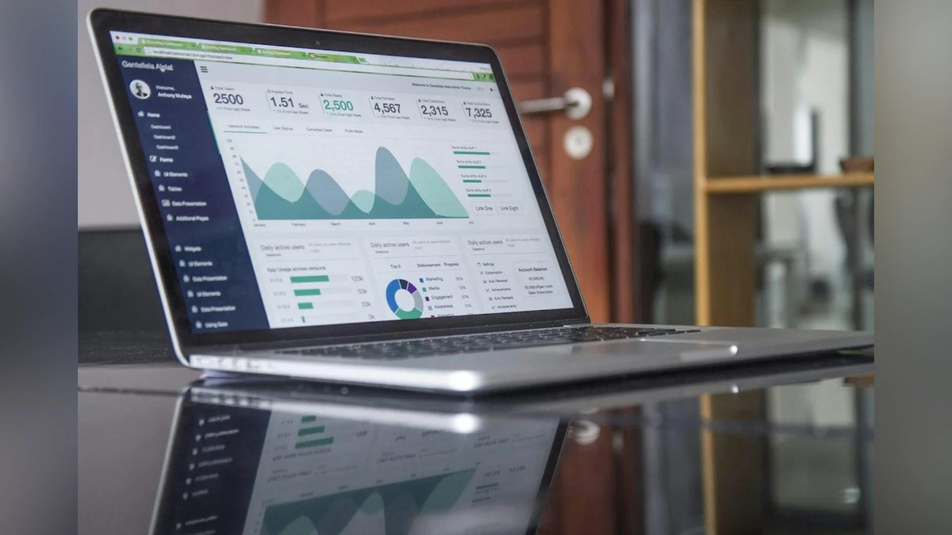 Side profile view of a laptop screen displaying a web analytics dashboard with performance graphs, line charts, and data metrics reflected on a glass tabletop.